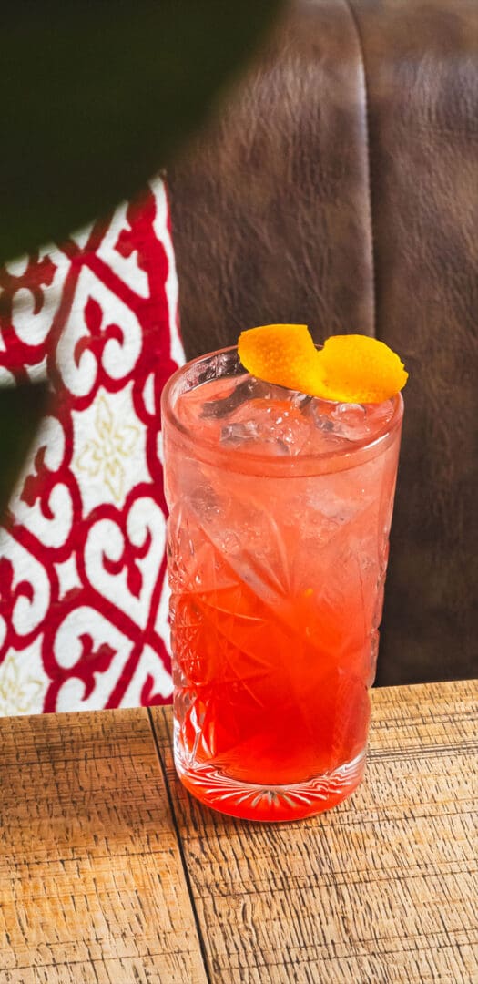 Cocktail rosso ghiacciato con twist d'arancia su tavolo in legno